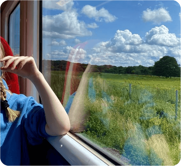 Person looking out of a train window at a green field and blue sky
